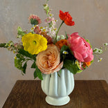 Colorful flower arrangement in a light green vase on a wooden surface with a neutral background