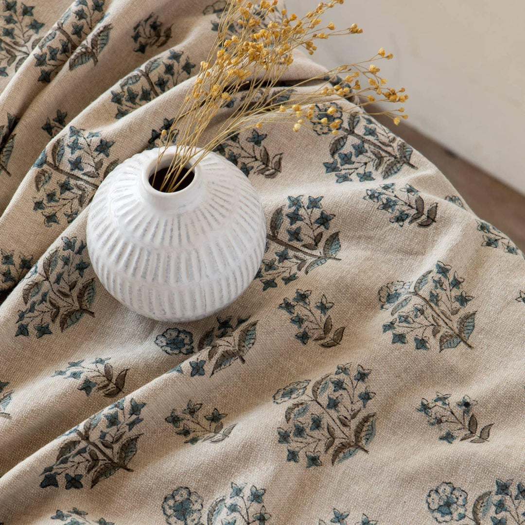 Floral-patterned fabric with a white vase and dried flowers on a wooden surface.
