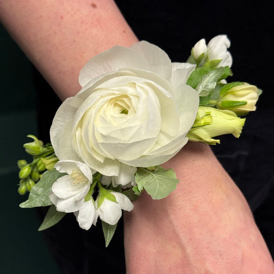 White floral corsage on a wrist with a plain background