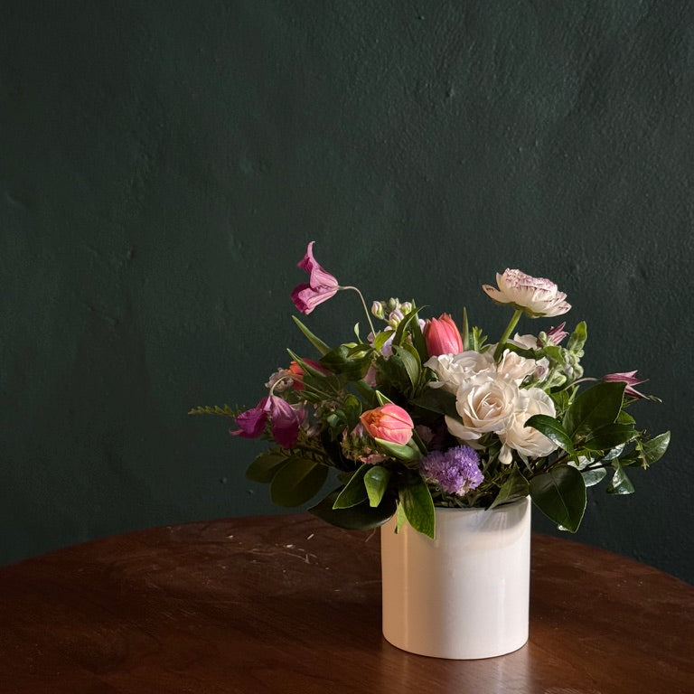 Floral arrangement in a white vase on a wooden table with a dark background