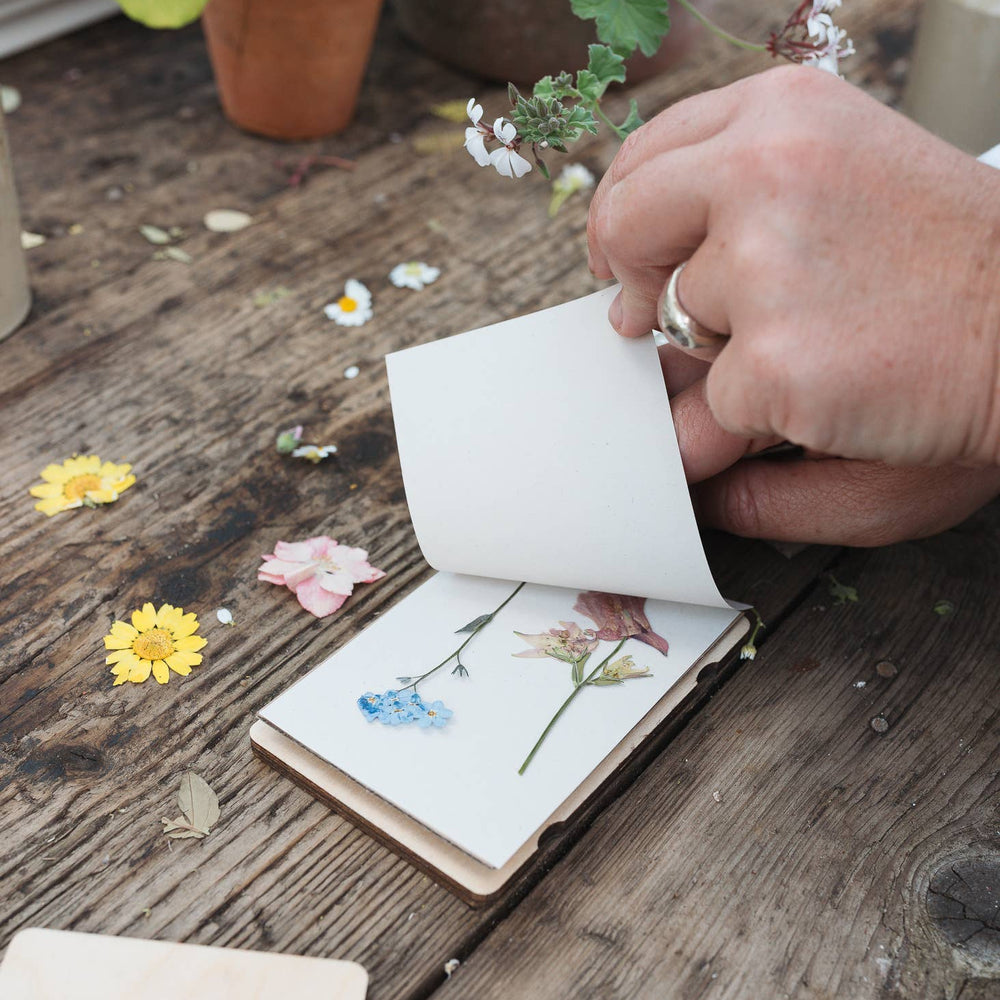 Person opening a small notebook with pressed flowers on a wooden surface