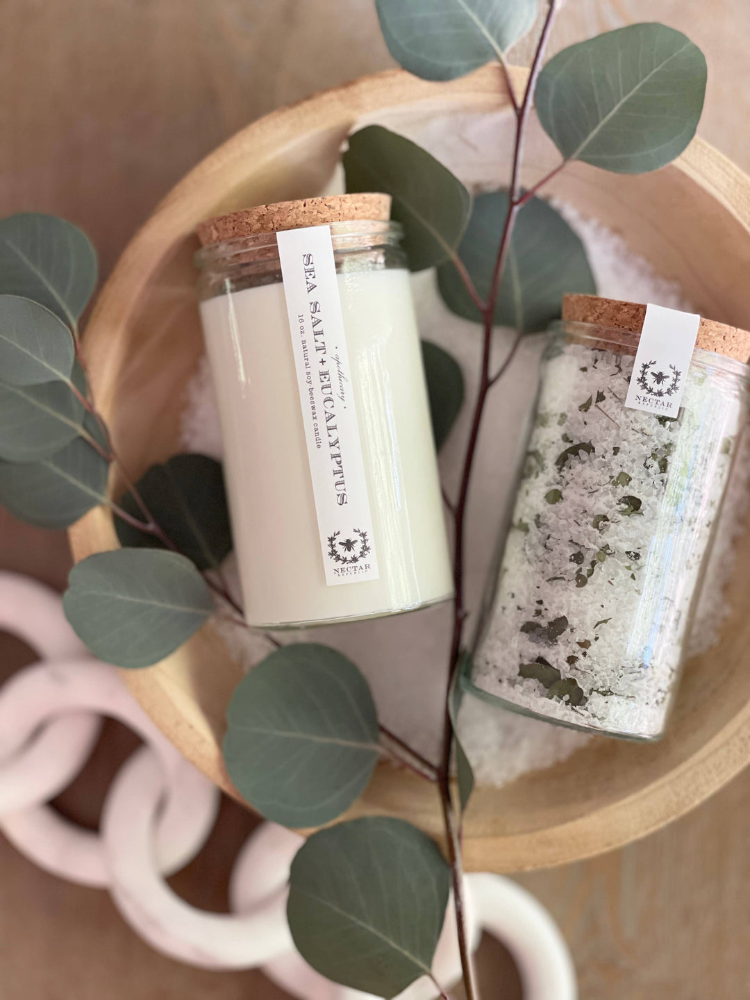 Two jars with labels on a wooden surface with green leaves.