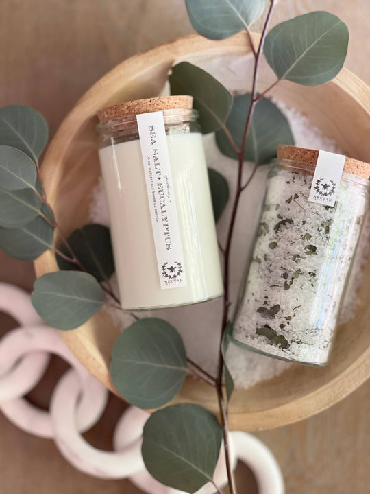 Two jars with labels on a wooden surface with green leaves.