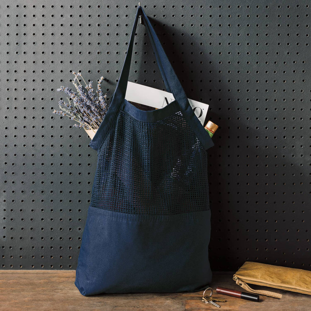 Blue tote bag with a textured top section and plain bottom section, hanging on a pegboard wall.