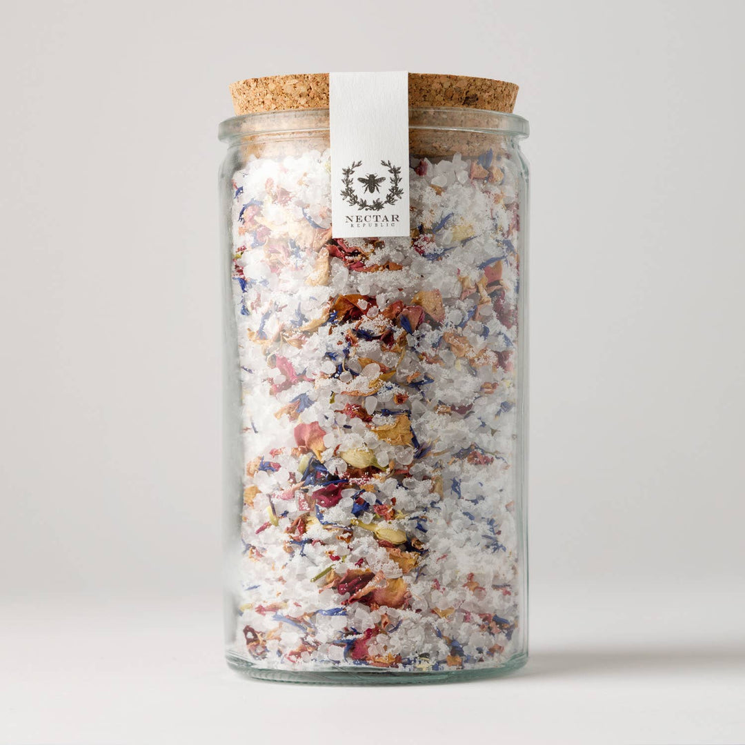 Glass jar with cork lid filled with colorful bath salts on a white background