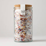 Glass jar with cork lid filled with colorful bath salts on a white background