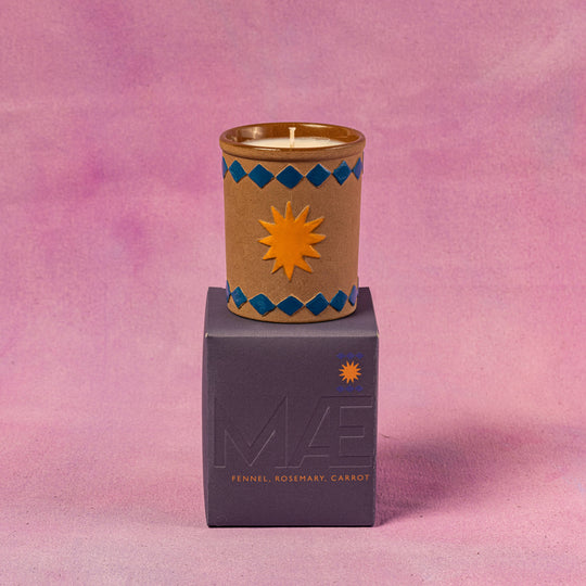 Candle in a decorative container on top of a purple box with 'MIZ' branding against a pink background