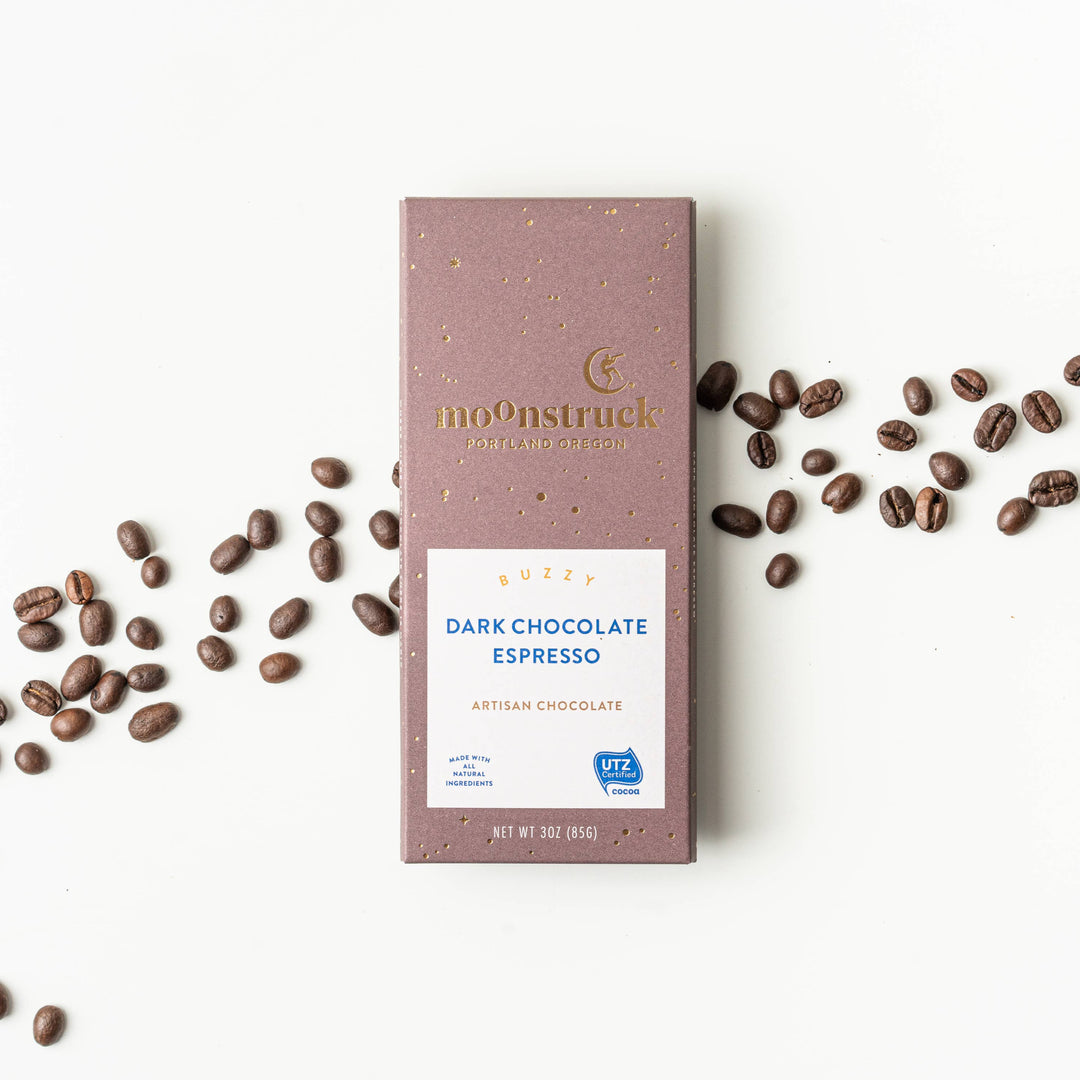Moonstruck Dark Chocolate Espresso bar with scattered coffee beans on a white background