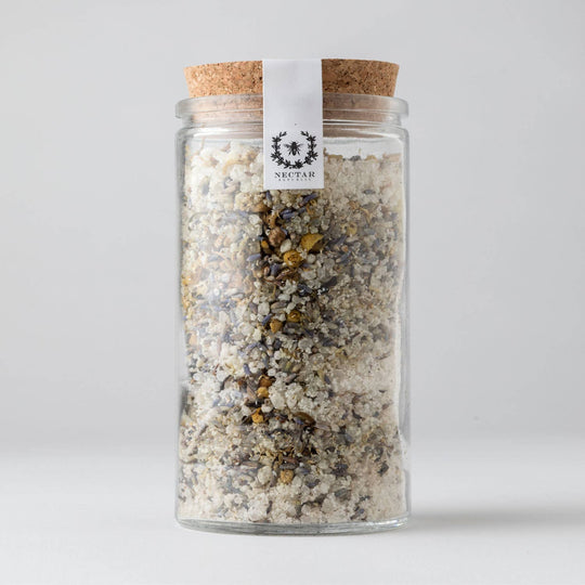 Glass jar with cork lid containing a mix of herbs or spices, on a light gray background.
