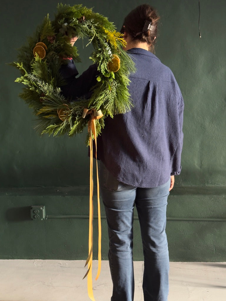 Person holding a large green wreath against a green wall