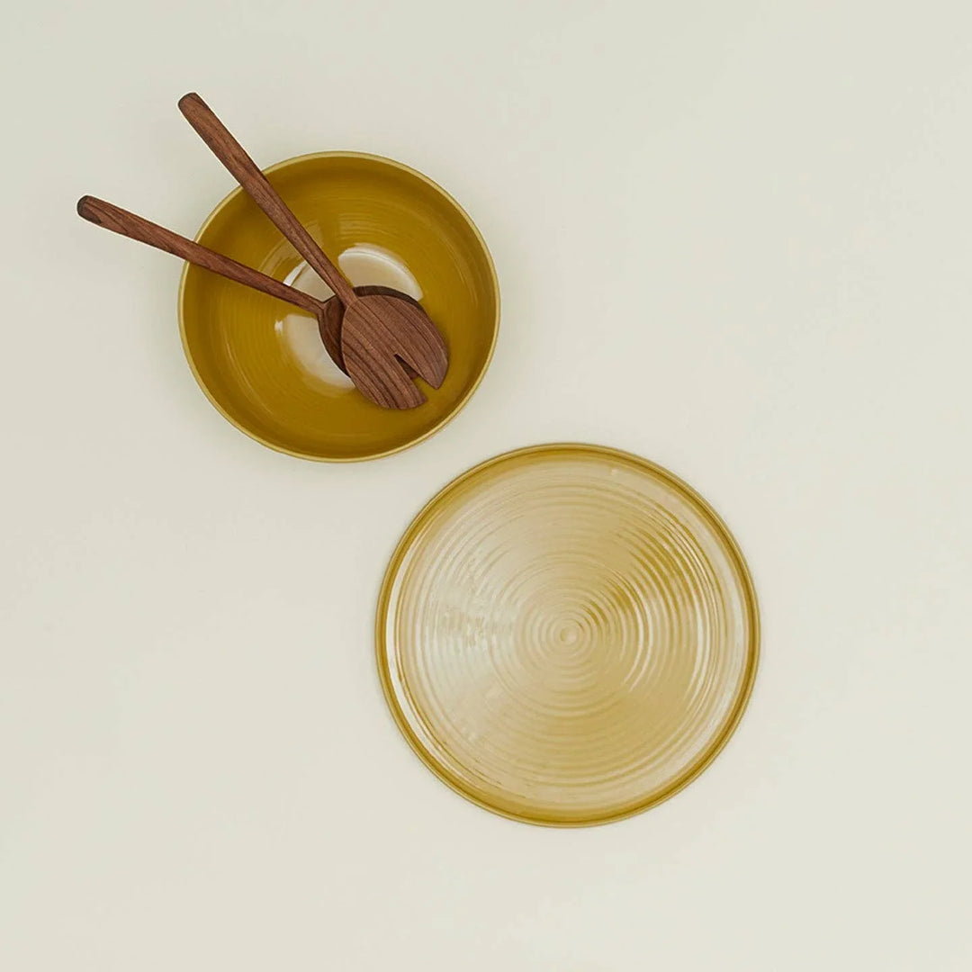 Mustard yellow ceramic bowl with wooden salad servers and matching plate, minimalist tableware set