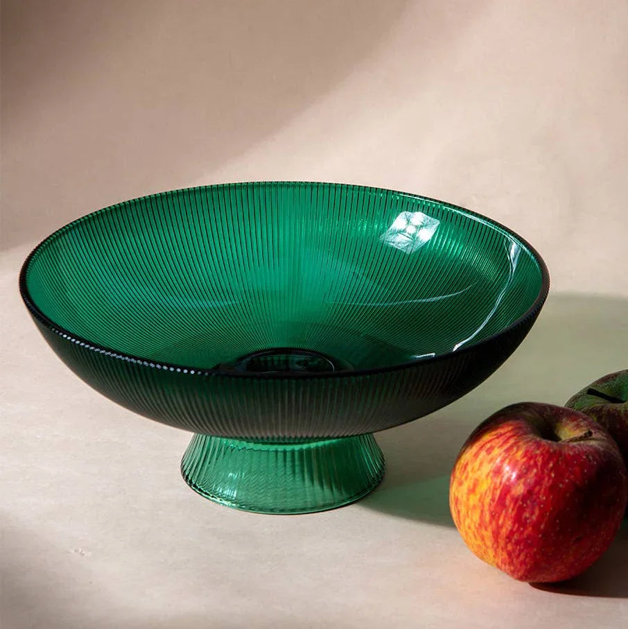 Green glass bowl on a beige surface with an apple beside it