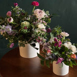Two flower arrangements in white vases on a wooden surface with a dark background