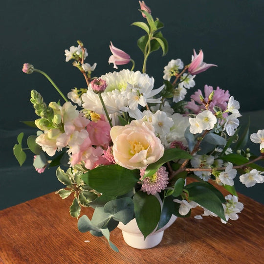 Bouquet of flowers in a white vase on a wooden surface with a dark background