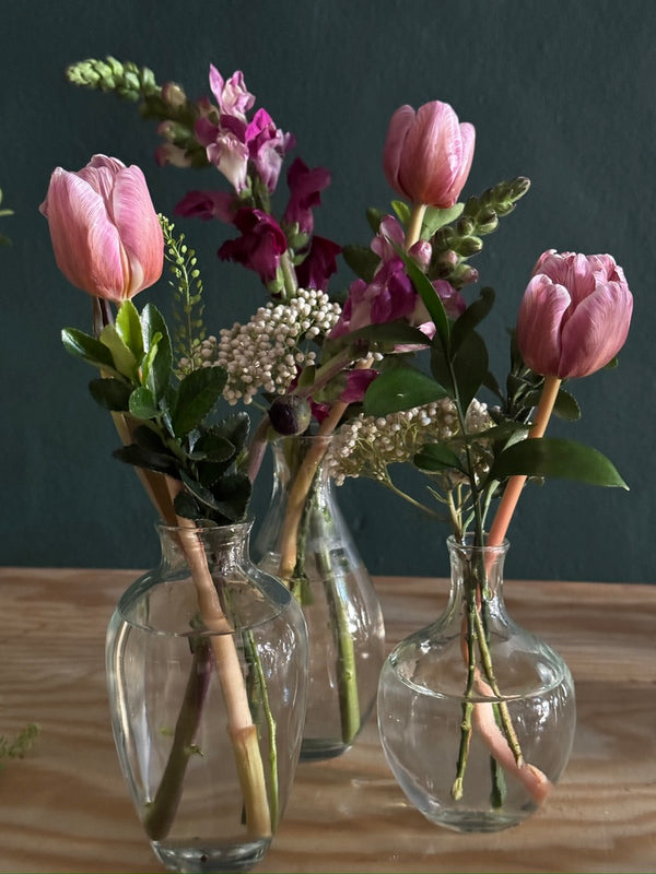 Three glass bud vases with pink tulips and seasonal stems for wedding and event tables
