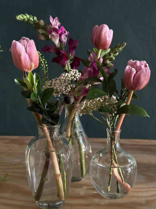 Three glass bud vases with pink tulips and seasonal stems for wedding and event tables