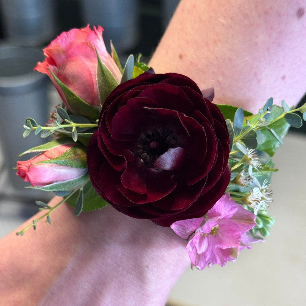 Floral wrist corsage with pink and dark red flowers on a wrist.