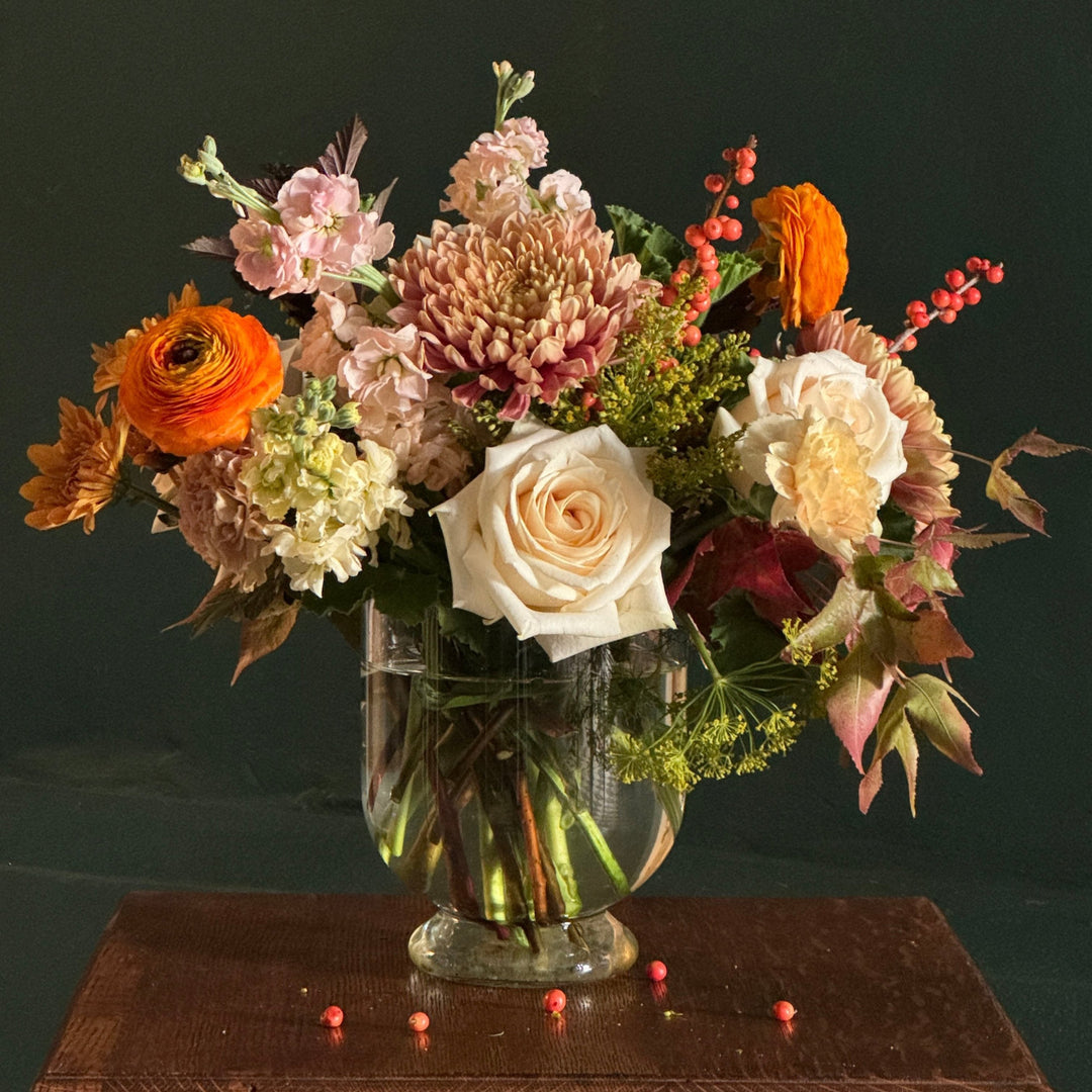 A footed glass vase with seasonal flowers arranged in a 360 degree design