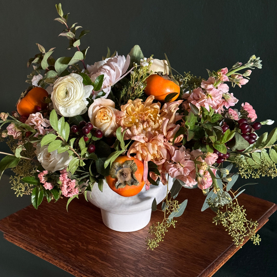 Bouquet of flowers with pumpkins and a white candle on a wooden surface against a dark background