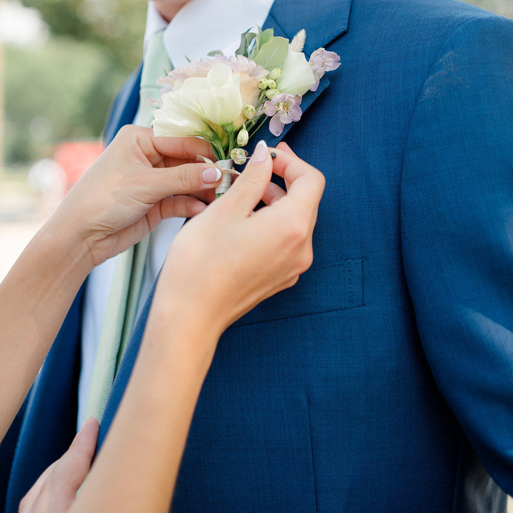 Person adjusting a floral boutonniere on a blue suit jacket.