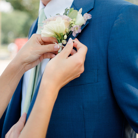 Person adjusting a floral boutonniere on a blue suit jacket.