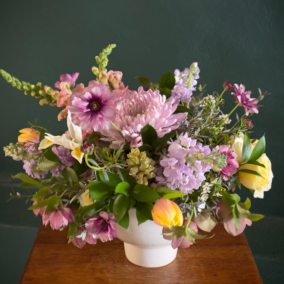 Floral arrangement in a white vase on a wooden surface with a dark background