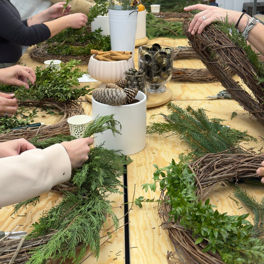 People making wreaths at a craft workshop with materials on a table.