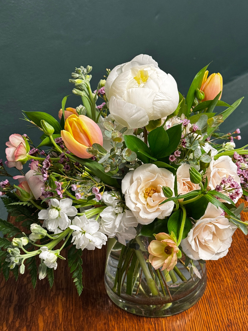 Bouquet of flowers in a clear vase on a wooden surface with a dark background