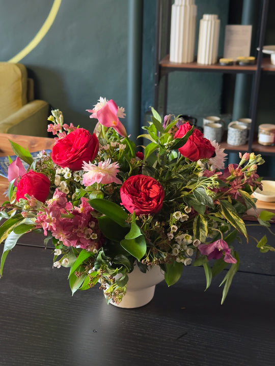 Bouquet of red and pink flowers in a white vase on a dark surface with a blurred background.