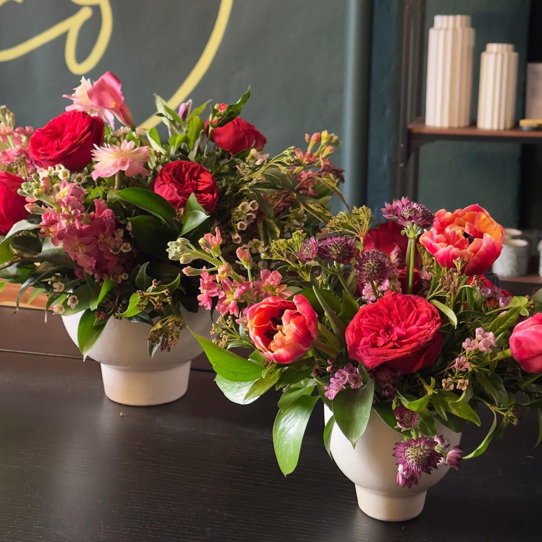 Three flower bouquets in white vases on a dark surface with a decorative background.