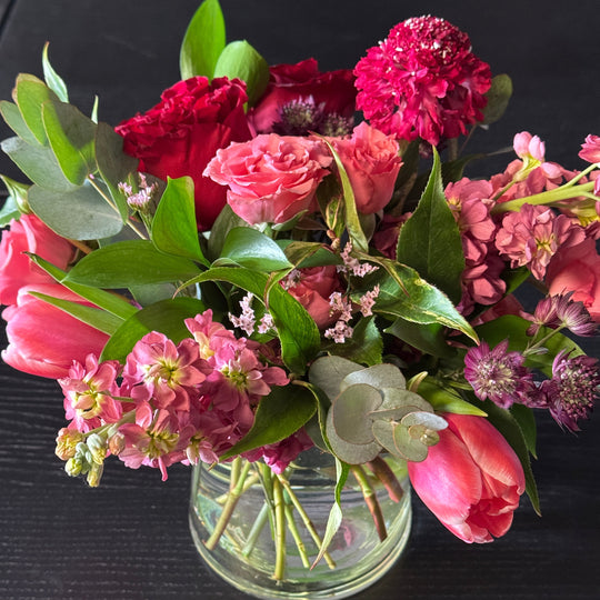 Bouquet of pink and red flowers with a glass vase on a dark surface