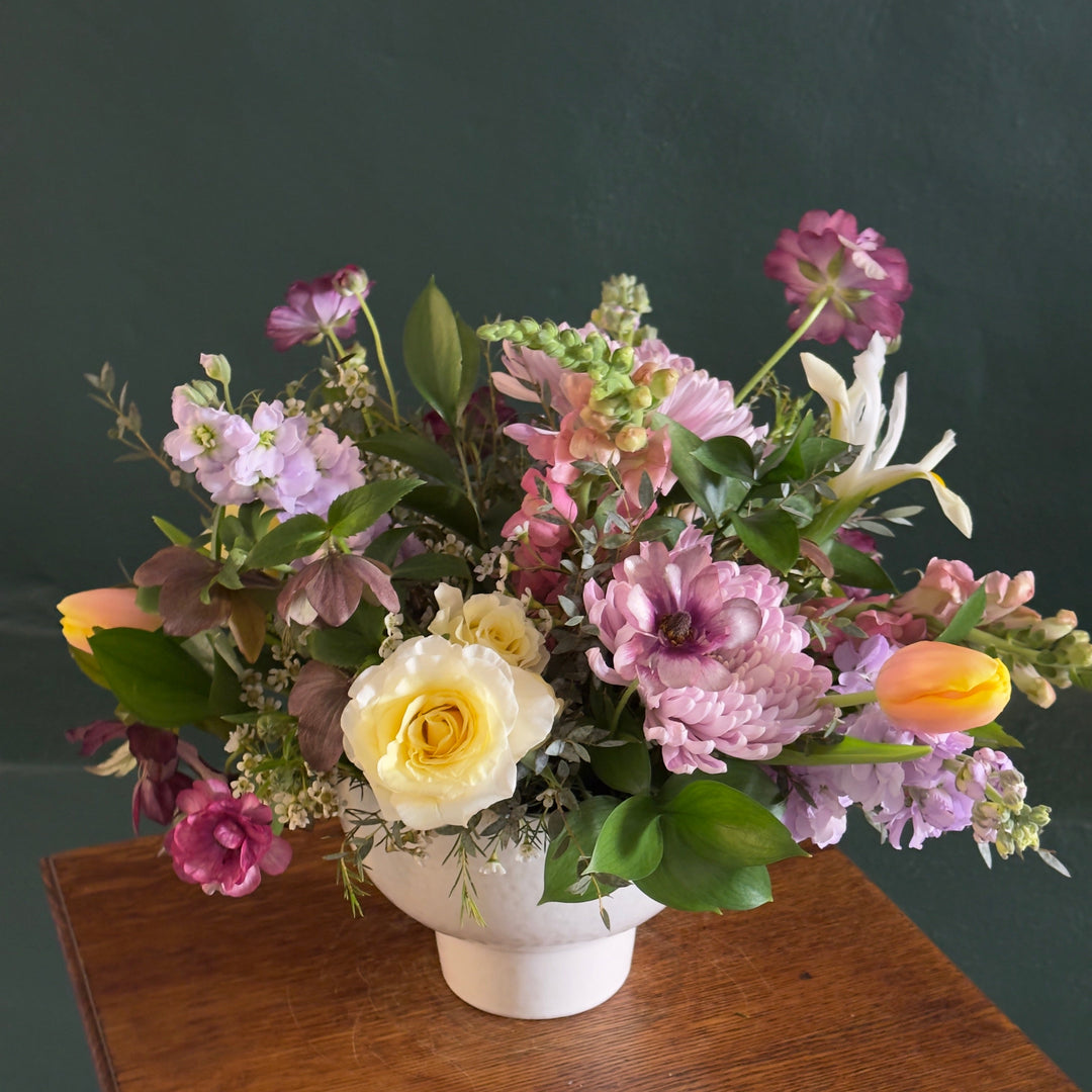 Floral arrangement in a white vase on a wooden surface with a dark background