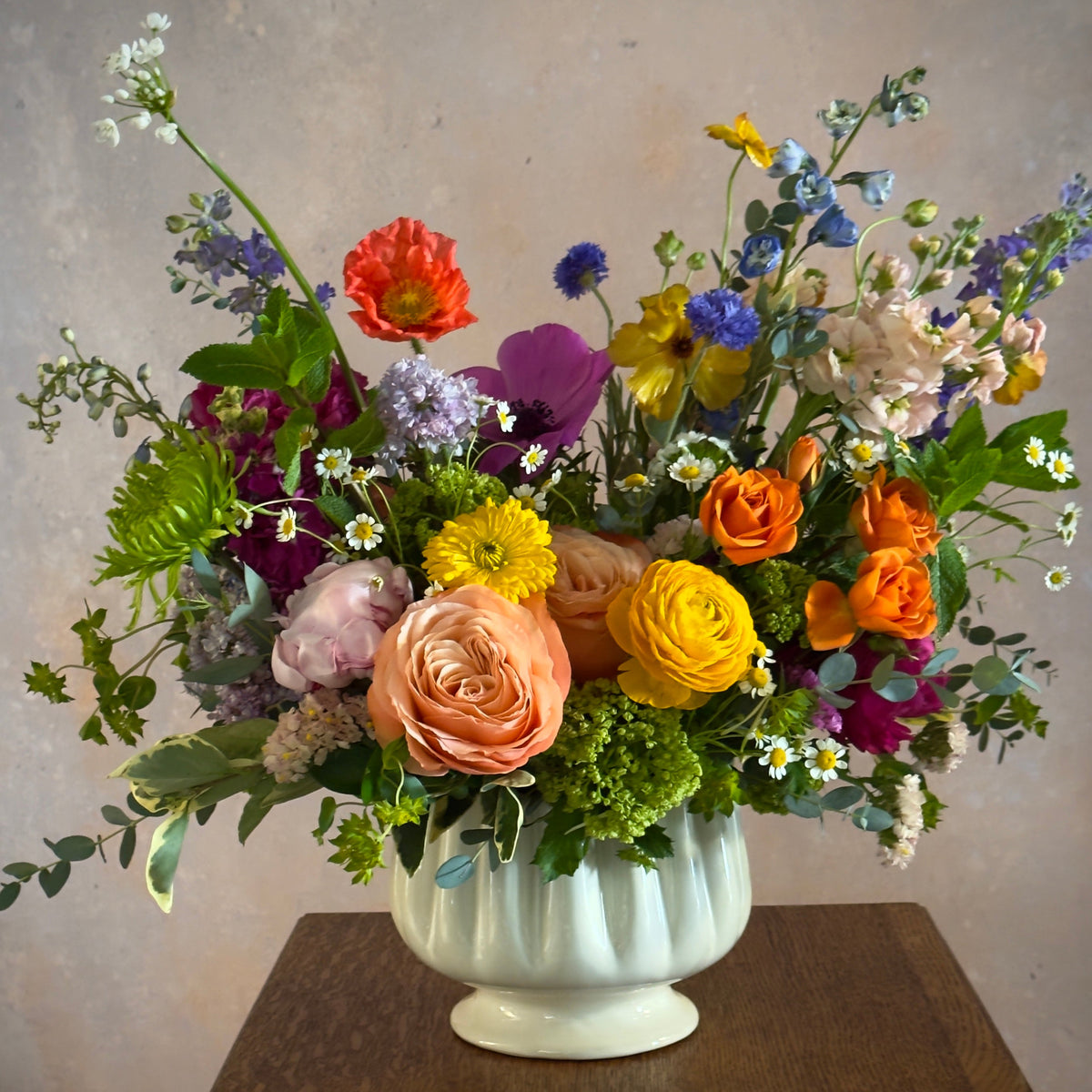 bright flowers in peaches, purples, blues, and greens in a white ceramic vessel. 