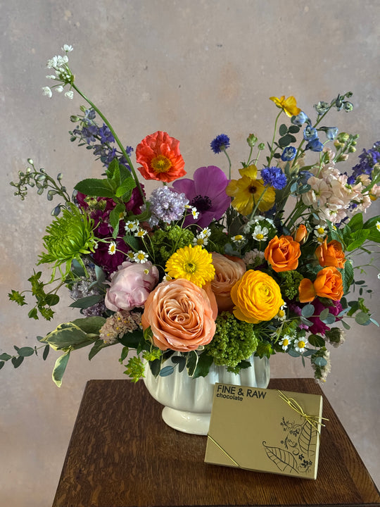 Colorful flower arrangement in a white vase on a wooden surface with a card.