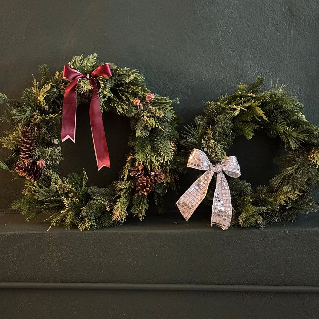 Two holiday wreaths of mixed wintery greens with bows and pinecone accents. Two sizes, 18" round and 14" round