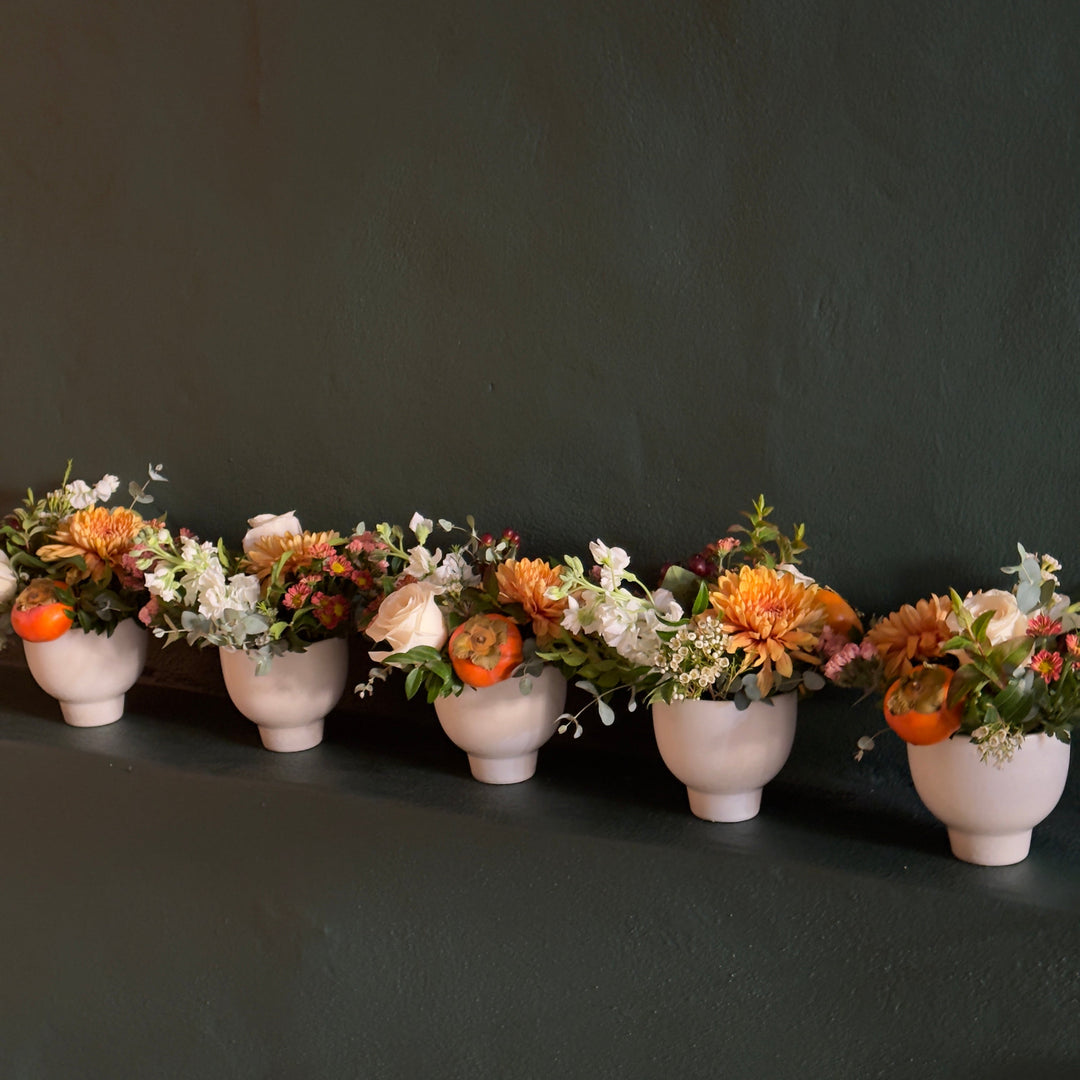 Row of small floral arrangements in white pots against a dark background