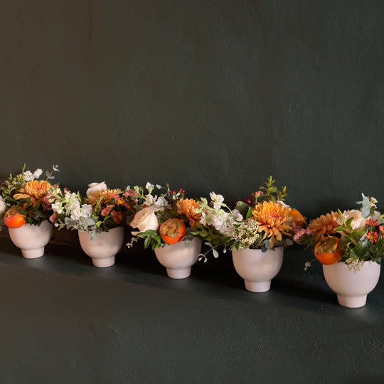 Row of small floral arrangements in white pots against a dark background