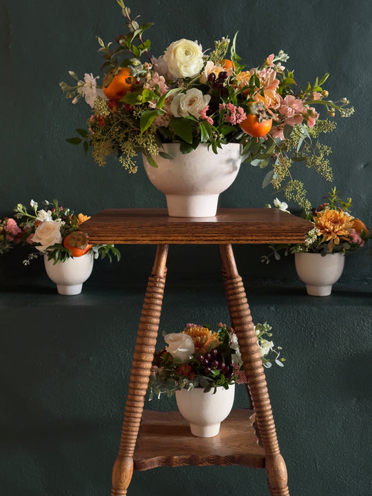 Floral arrangement in a white vase on a wooden ladder against a dark background