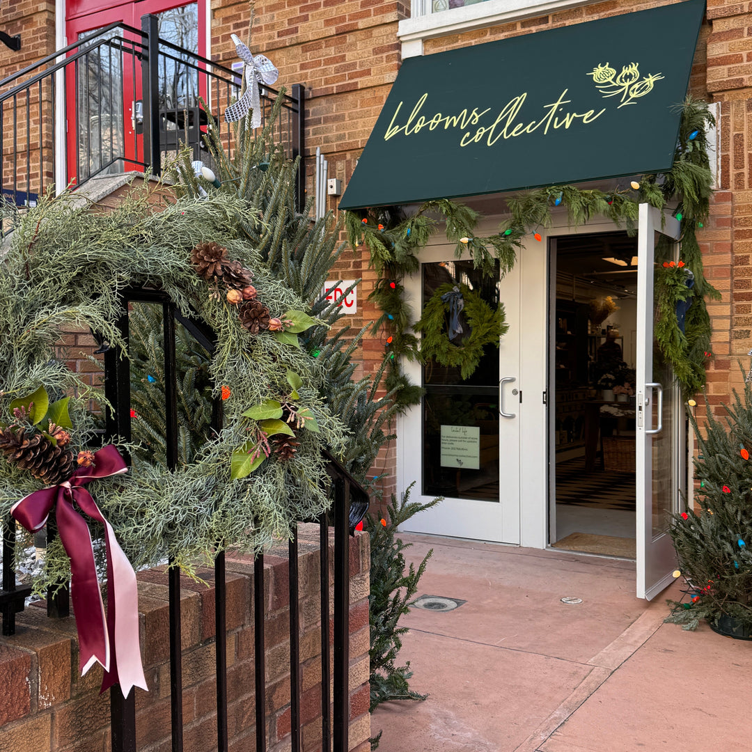 Decorative wreath with greenery and a pink bow in front of a building entrance.