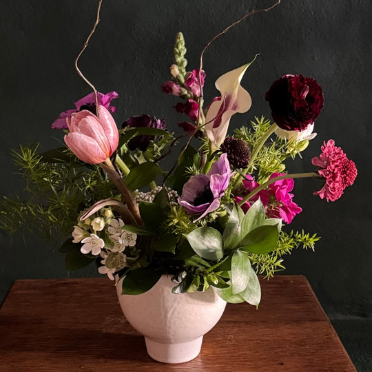 Floral arrangement in a white vase on a wooden surface with a dark background