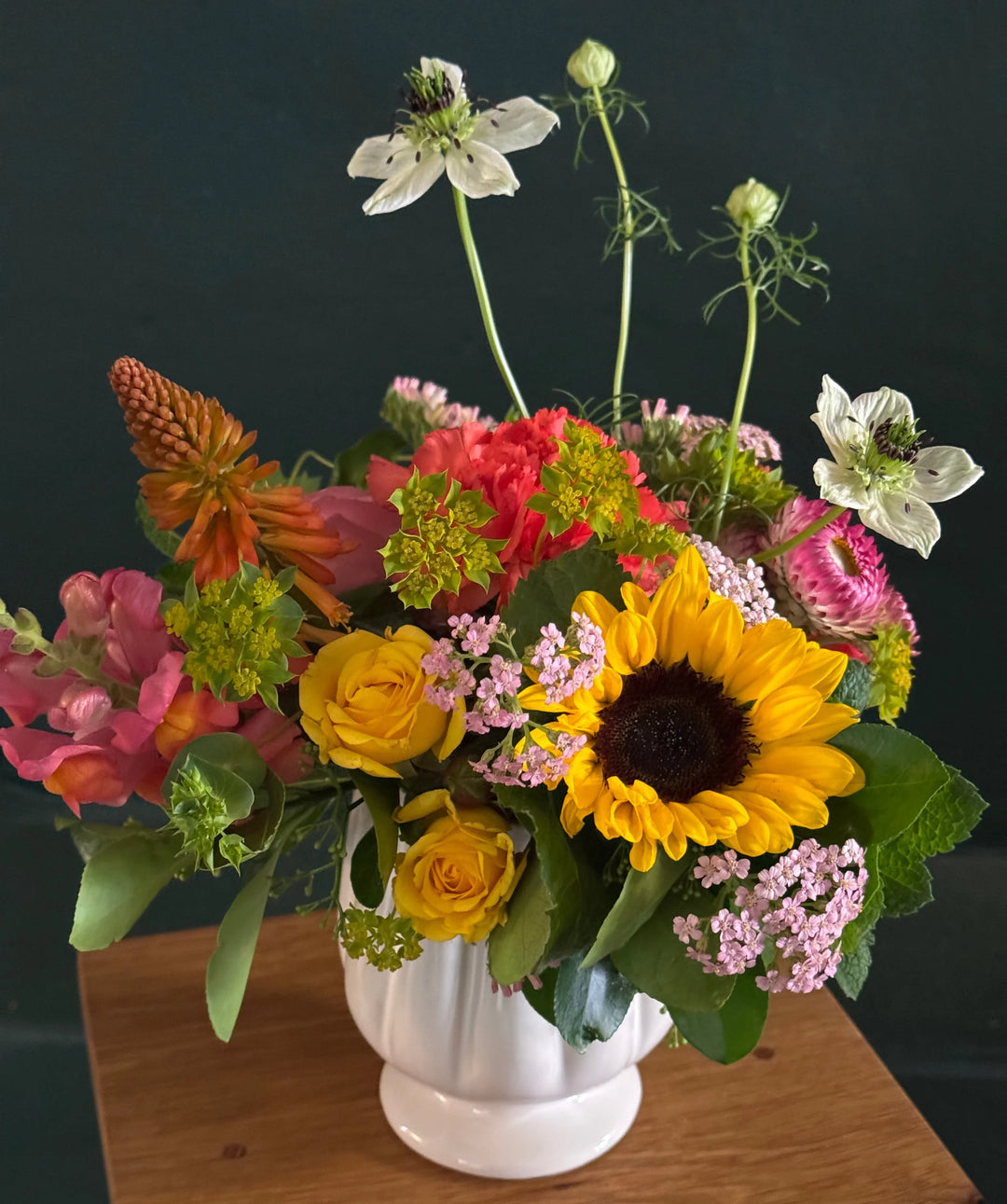 Colorful flower arrangement with sunflowers and roses in a white vase on a wooden surface.
