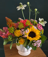 Colorful flower arrangement with sunflowers and roses in a white vase on a wooden surface.