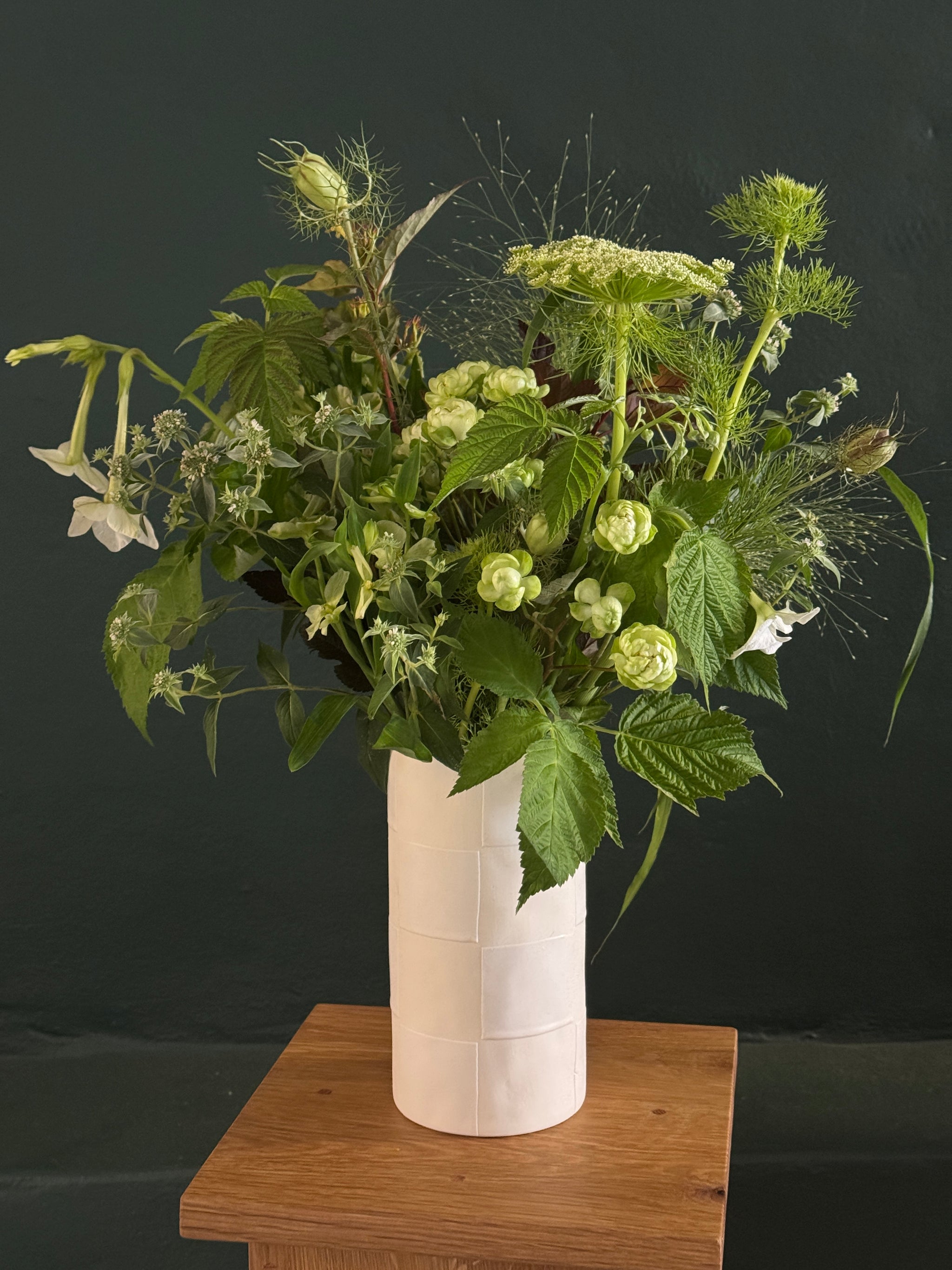 flower arrangement of green grasses, millets and lace flowers in a white vase