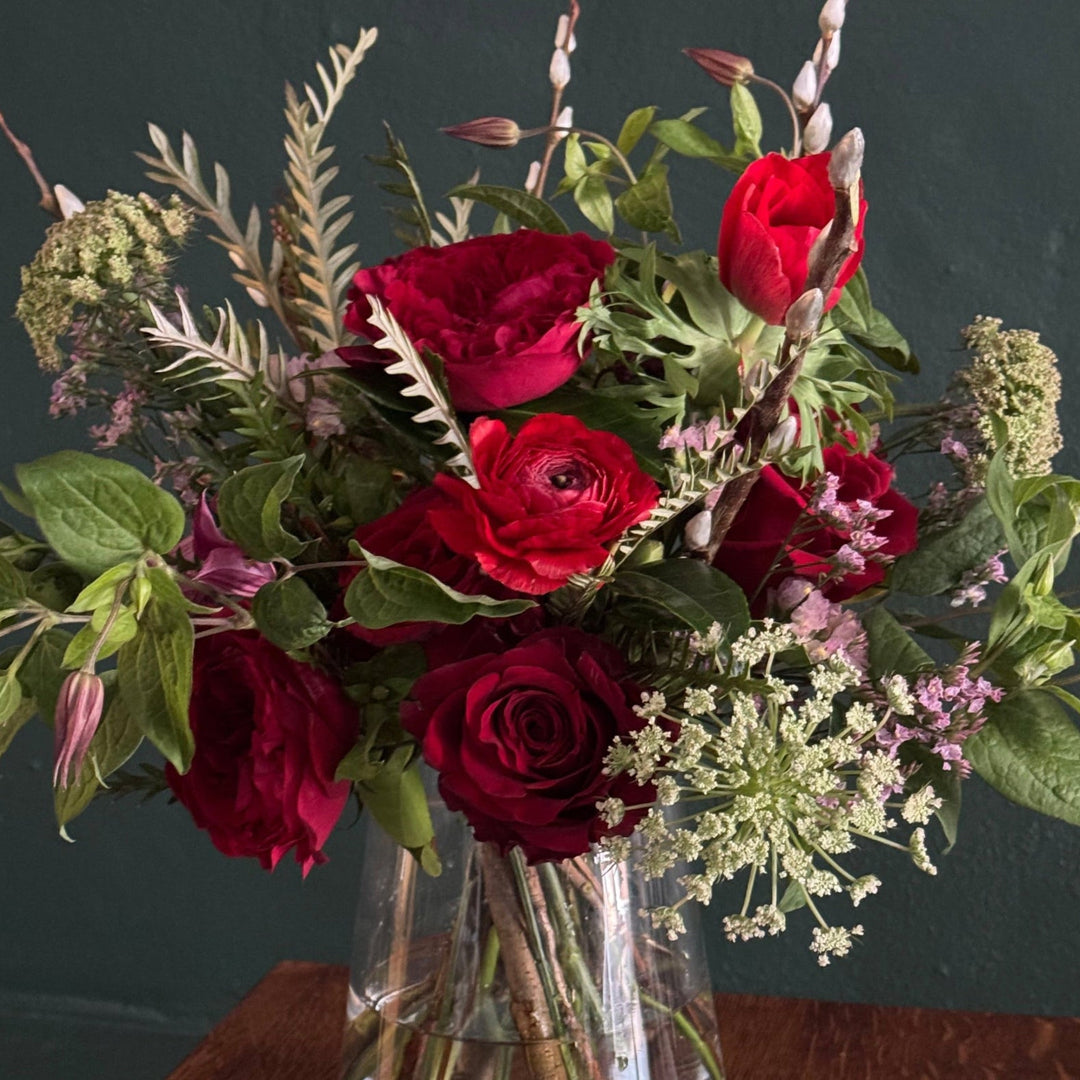 Bouquet of red roses and greenery in a clear vase against a dark background