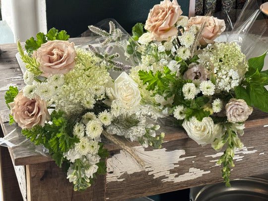 Two floral arrangements with blush pink roses, white roses, and green foliage displayed on a rustic wooden table.