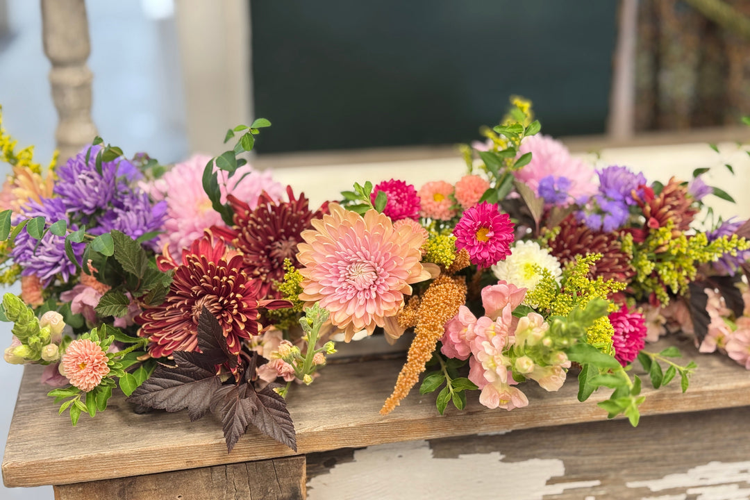 A colorful faux floral garland with pink, purple, orange, red, and yellow flowers, displayed on a rustic wooden table.