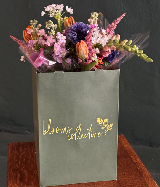 extra large bouquet of flowers in pinks, purples and orange , spiraled and hand-tied  and inside a green bag with Blooms Collective logo