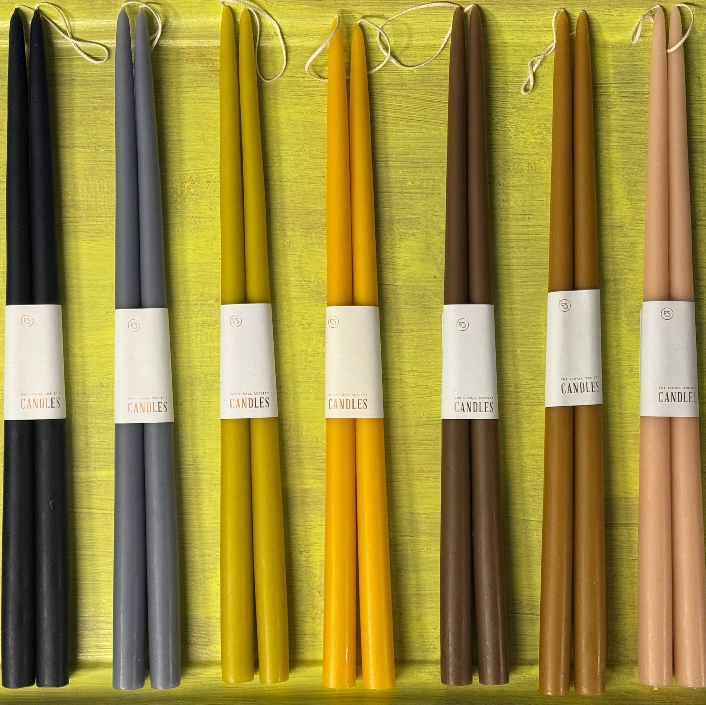 A set of 18-inch dipped taper candles in various colors including black, gray, yellow, and brown, with labels attached.