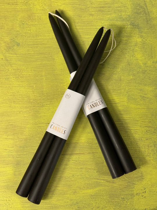Two black candles with white labels on a green wooden surface.
