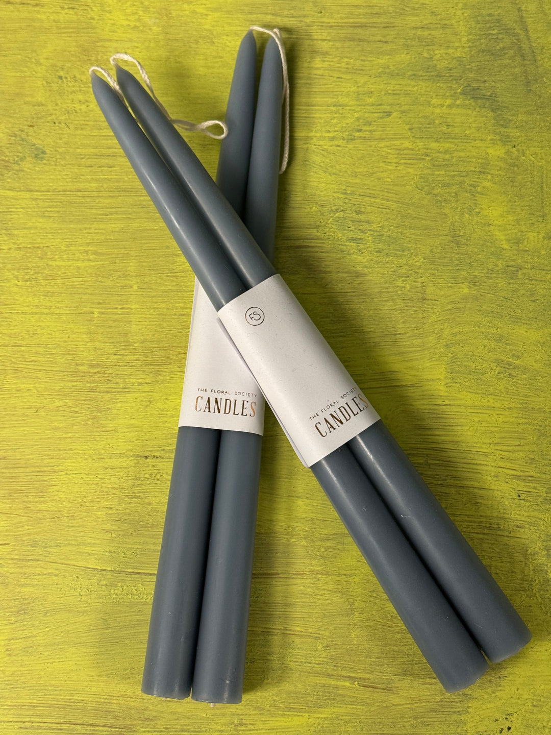 Light blue taper candles with packaging on a green wooden surface